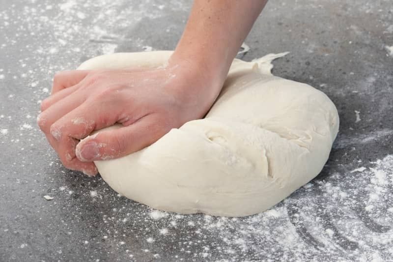 Hand knådar en mjuk vetedeg på ett mjölat bakbord